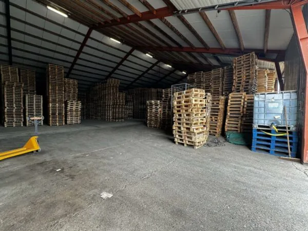 Houten pallets zijn opgestapeld in een grote loods aan de Graaf van Lynden van Sandenburgweg.
